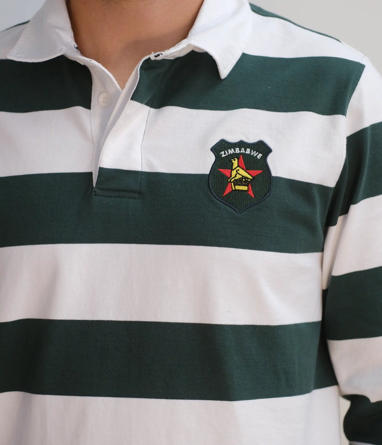 Close-up of the Zimbabwe rugby jersey collar, featuring white cotton twill, inner Sables-branded neck tape, and an embroidered Zimbabwe badge on green and white horizontal stripes.